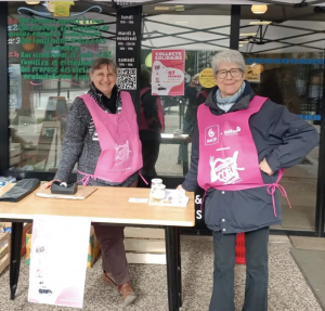 Deux bénévoles de Ma P'tite Echoppe en tablier rose des Restos du coeur attendant les dons devant l'épicerie.
